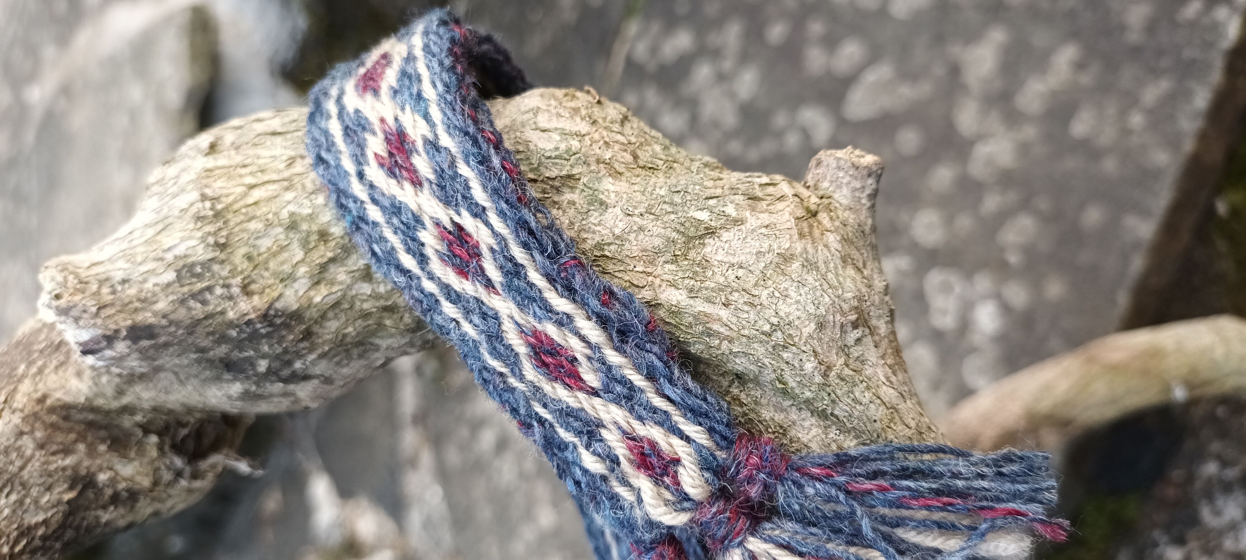 Blue, cream and burgundy card woven band wrapped around a tree branch