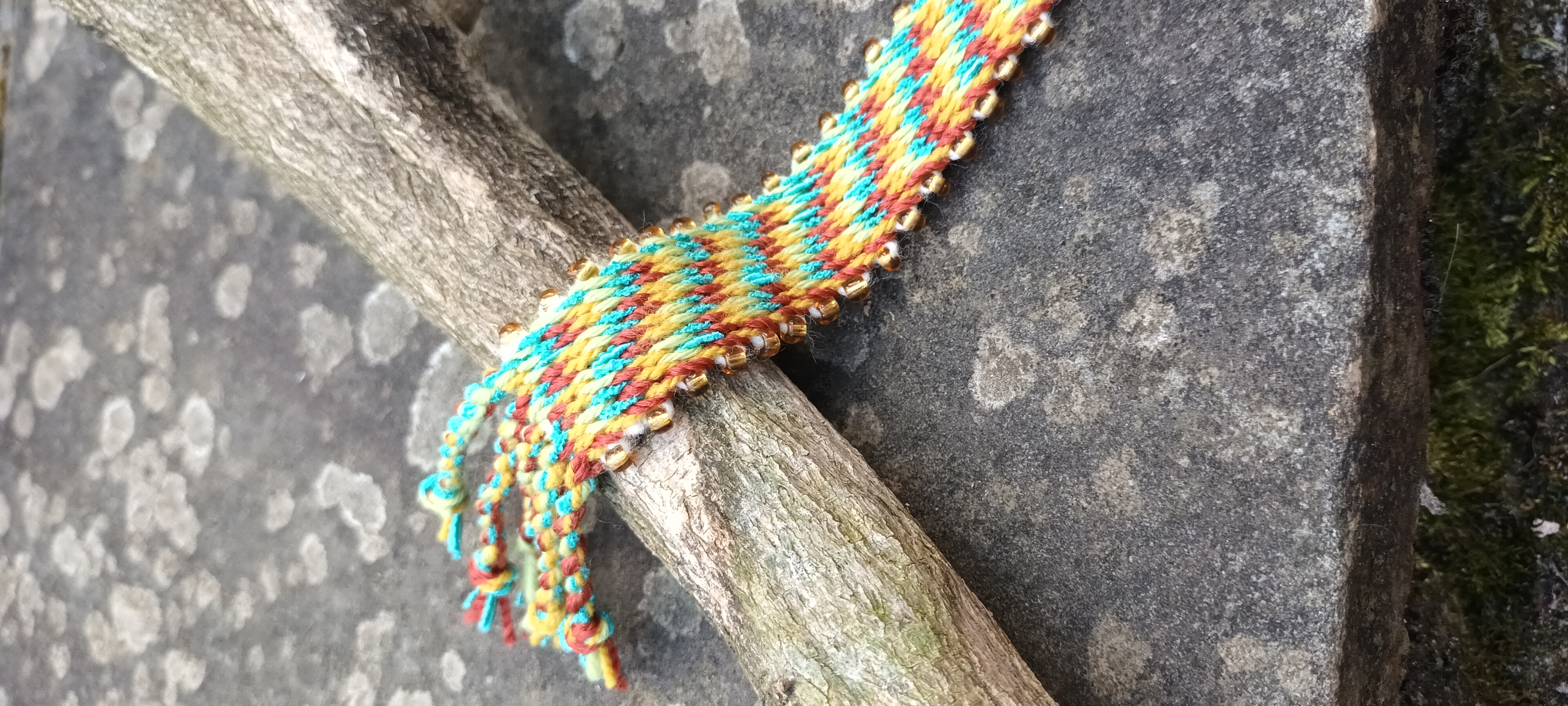 Bright yellow, turquoise and red card woven band with gold beads along the edges