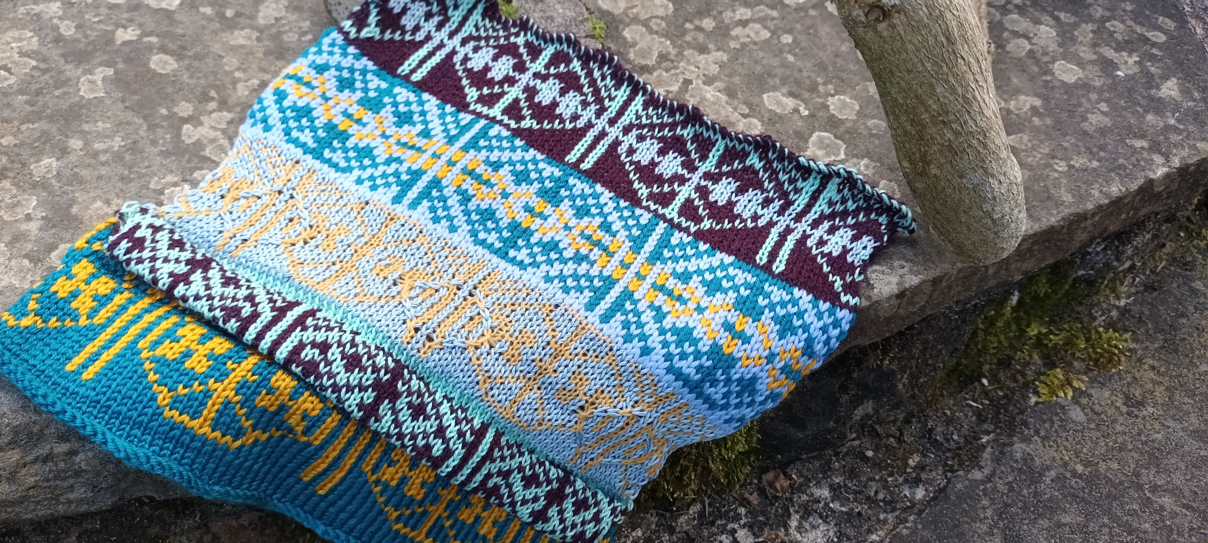 Blue, teal, gold and purple Fairisle knitted sample on stone
